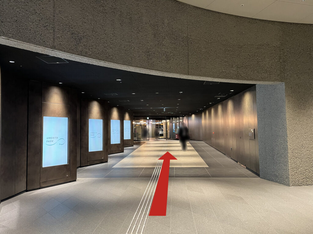 Signature グラングリーン ゲートタワーへのアクセス：通路沿いにあるデジタルサイネージの横をまっすぐに伸びる矢印　正面に自動ドア