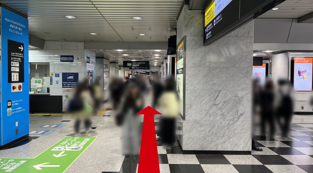 御堂筋口改札を出て左に向いた通路の様子。左側には青い柱や改札があり、天井には蛍光灯が並び、前方奥には外の明かりが見える出口が続いています。