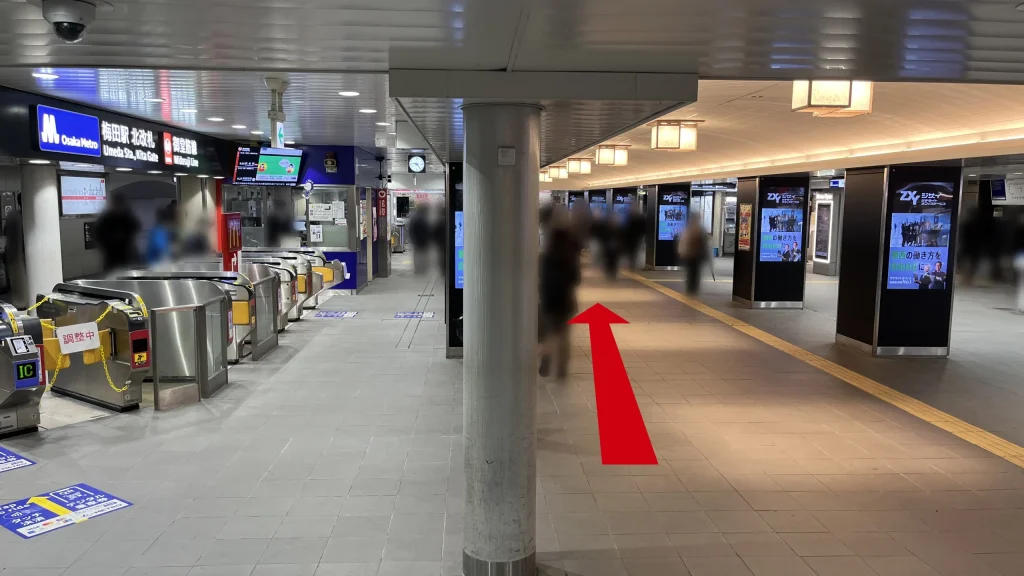 Alt：Signatureグラングリーンゲートタワーへのアクセス方法：Osaka Metro御堂筋線梅田駅の北改札外通路で、左側にシルバーの自動改札機が並び、右側にデジタルサイネージの柱が連続して立っている様子。