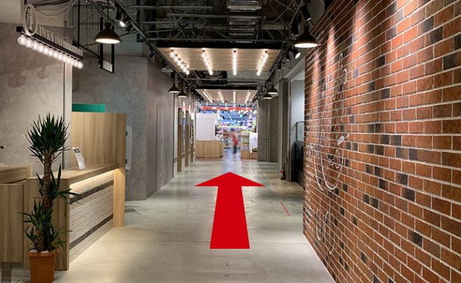 インフォメーションカウンターとレンガの壁の間の通路を直進しています