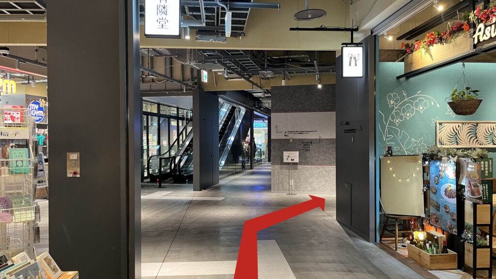 JAM BASEへのアクセス：グラングリーン大阪北館の館内を右に進み、左手にエスカレーター、右手にエレベーターホールが見える分岐点の写真　通路の両脇に有隣堂書店、右手に飲食店がある