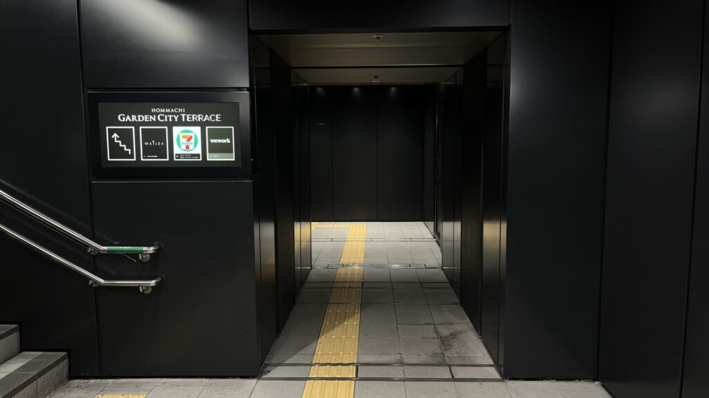 WeWork本町へのアクセス：左手に本町ガーデンシティテラスの案内看板、右手にエレベーターホールへ伸びる通路