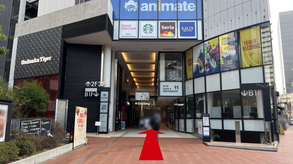 H¹O梅田茶屋町へのアクセス：NU茶屋町を正面から見た図　左手にオニツカタイガー、上の階にアニメイト、スターバックス、セリア、カルディ、左手にタワーレコードなどの看板が見える