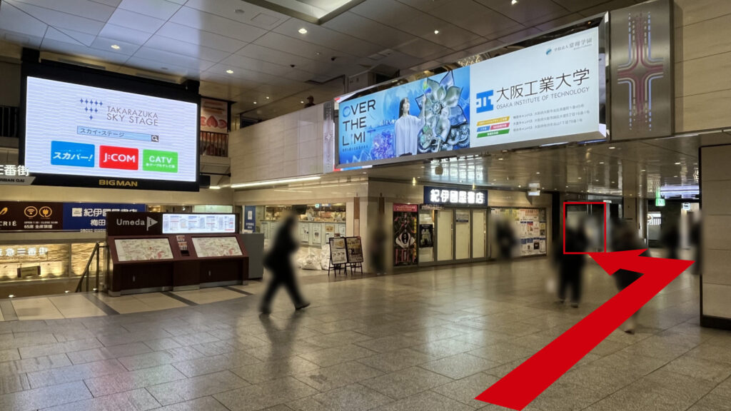 billage OSAKA 朝日プラザ梅田へのアクセス：左前方に巨大モニターBIGMANとその下に階段、右前方に通路上部に大きな広告、その下に紀伊国屋書店がある