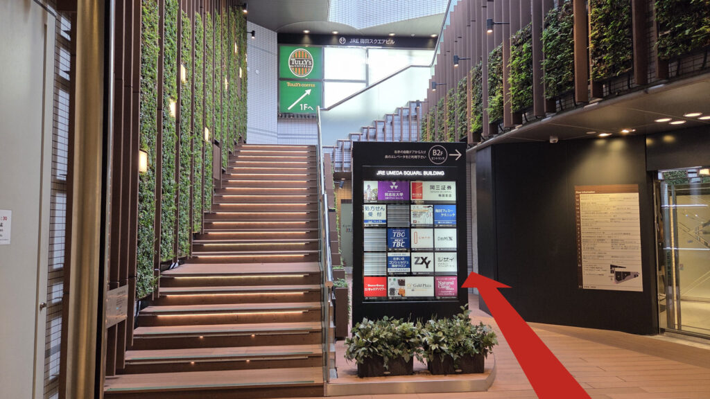 リージャス梅田スクエアビジネスセンターへのアクセス方法：JRE大阪連絡通路を入った先の風景　左側に螺旋状に伸びる階段、右側にビル地下入り口があり、中央にテナント看板がある