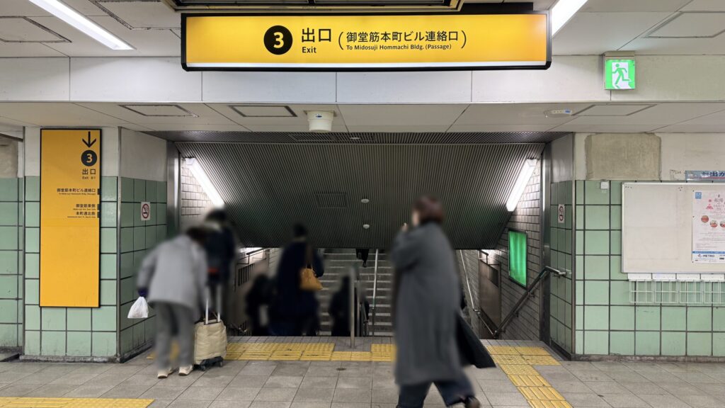 H¹O 本町へのアクセス：Osaka Metro 本町駅構内にある「3番出口（御堂筋本町ビル連絡口）」への階段と案内看板