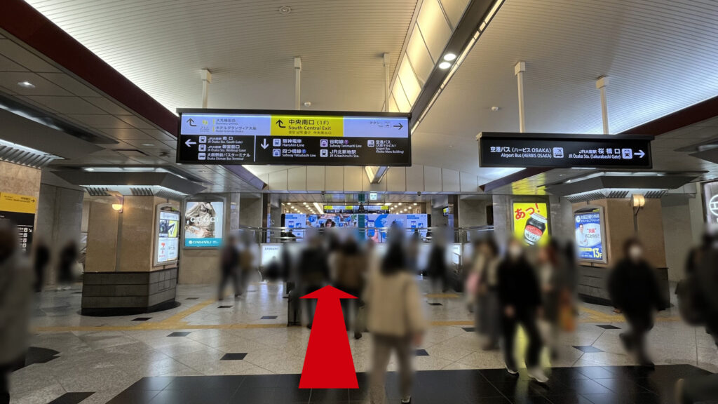 リージャス梅田スクエアビジネスセンターへのアクセス方法：天井から吊り下げられた黄色い「中央南口（1F）」の案内板と、その下にある地下へのエスカレーター入口