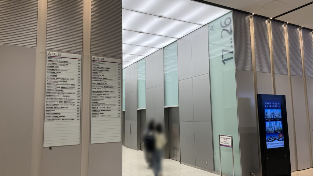 リージャス大阪梅田ツインタワーズ・ノースビジネスセンターへのアクセス：17階から26階へ繋がるAのエレベーターホール　エレベーターホールの手前左手にテナントの企業案内板が貼られており、右手にはデジタルサイネージが置かれている