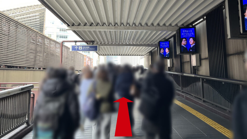 Compass Offices イノゲート大阪へのアクセス：「天ぷらまきの」の前を道なりに進んで屋外へ出た通路の図　前方に「↑JR大阪駅」と書かれた看板が見える　右手にはデジタルサイネージが並んでいる