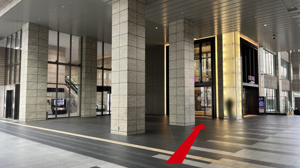 SHARE LOUNGE梅田 蔦屋書店へのアクセス：連絡橋口から「ルクアイーレ」入口へ続く通路。左手にはオフィスタワーがある。等間隔に大きな石柱が立っており、その先に光る柱とルクアイーレへの入り口がある