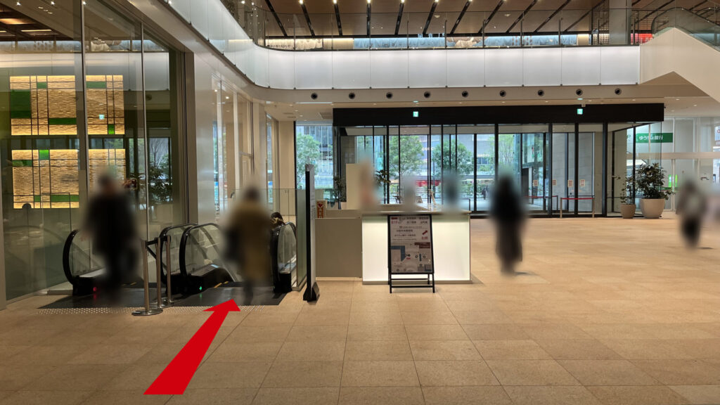 リージャスパシフィックマークス西梅田ビジネスセンターへのアクセス方法：「KITTE大阪」館内の地下へ続くエスカレーターの様子　前方にはKITTE大阪館内の吹き抜けと反対側にある1F出口が見える