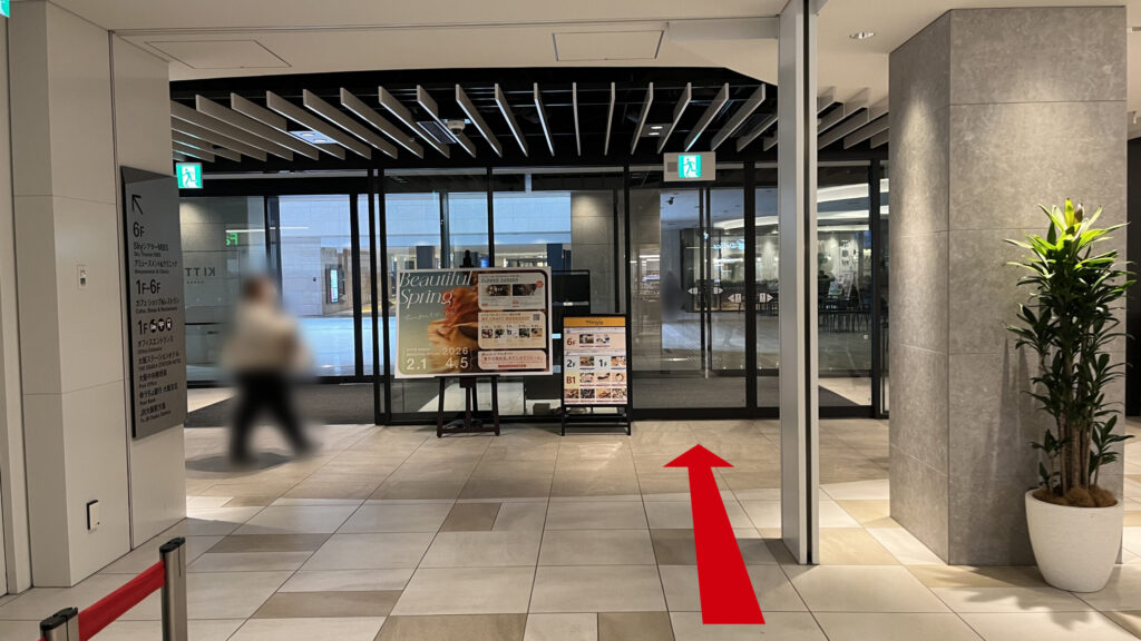 リージャスパシフィックマークス西梅田ビジネスセンターへのアクセス方法：地下の広々とした吹き抜け空間に向かって直進している様子　前方に自動扉が二つあり、その手前右手には大きな灰色の柱が立っている