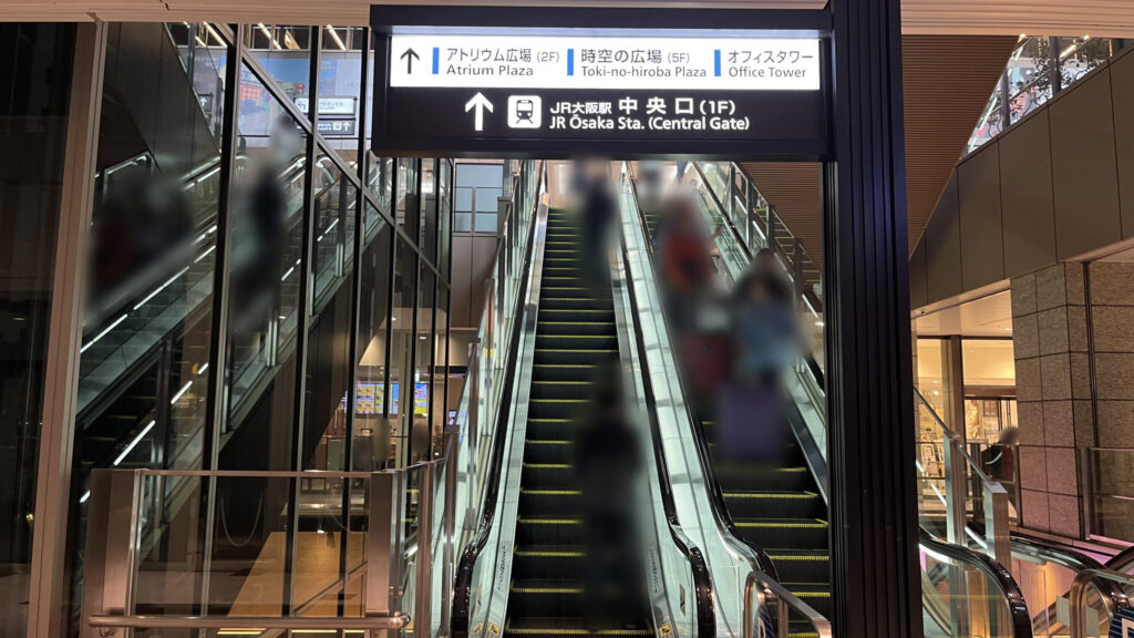 Compass Offices イノゲート大阪へのアクセス方法：上りエスカレーターの乗り口を正面から見た図　JR大阪駅中央口の矢印が書かれた看板が頭上に配置されている