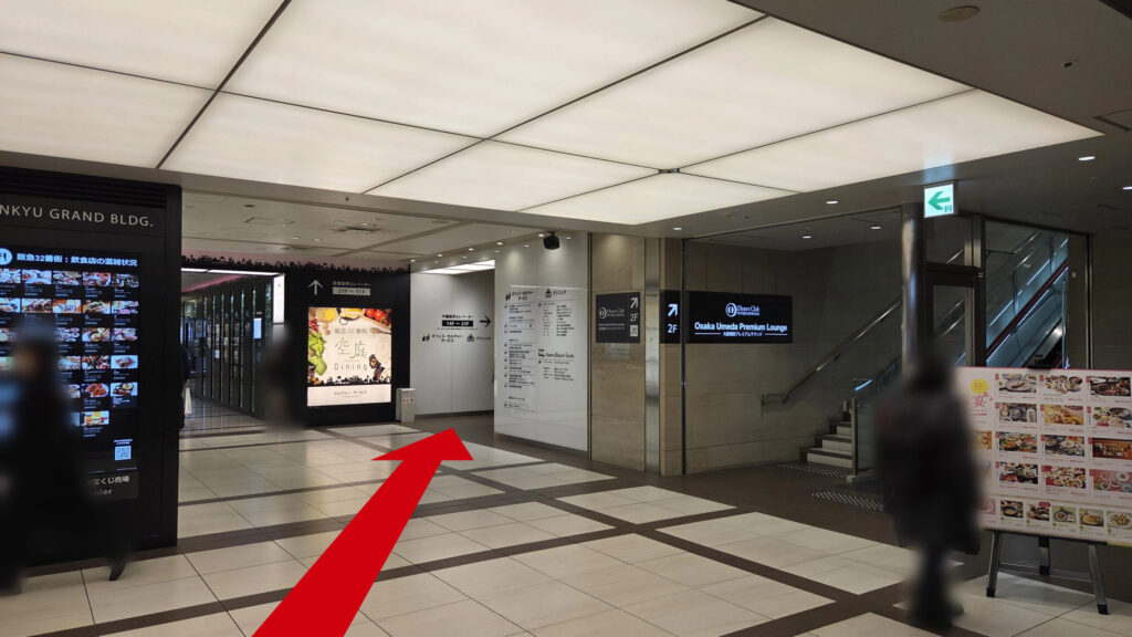 リージャス梅田阪急グランドビルビジネスセンターへのアクセス方法：ビル内部のフロア。天井の照明パネルが明るく、壁面にはエレベーターの方向を示す矢印がある。