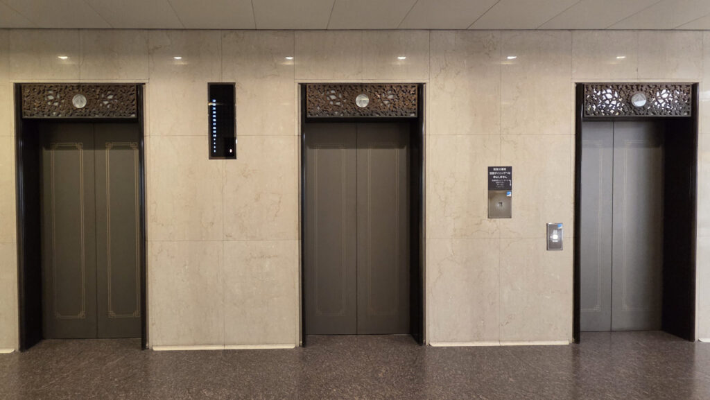 リージャス梅田阪急グランドビルビジネスセンターへのアクセス方法：大理石調の壁面に、上部に装飾が施されたエレベーターが並んでいる様子。