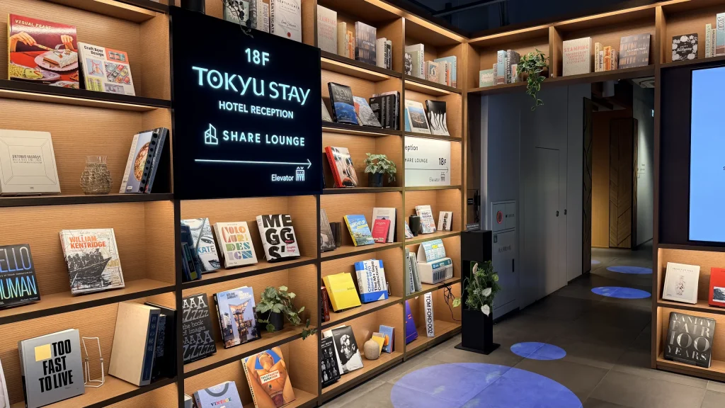 18Fのフロントとシェアラウンジを案内する電光掲示板と、本棚に囲まれた1Fロビー。