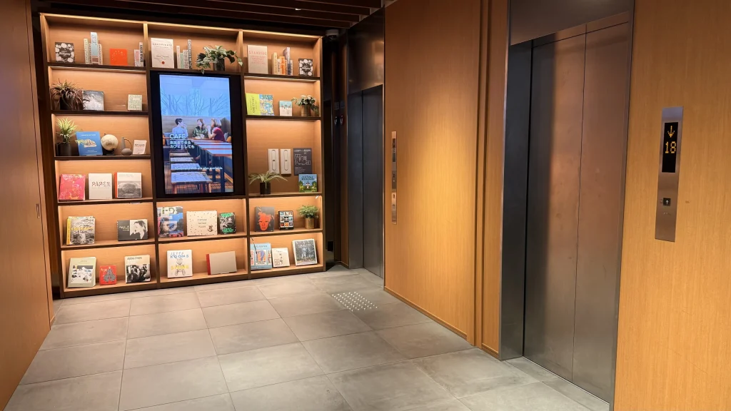 1Fのエレベーターホール。木目調の壁面にデジタルインフォメーションが設置されている。