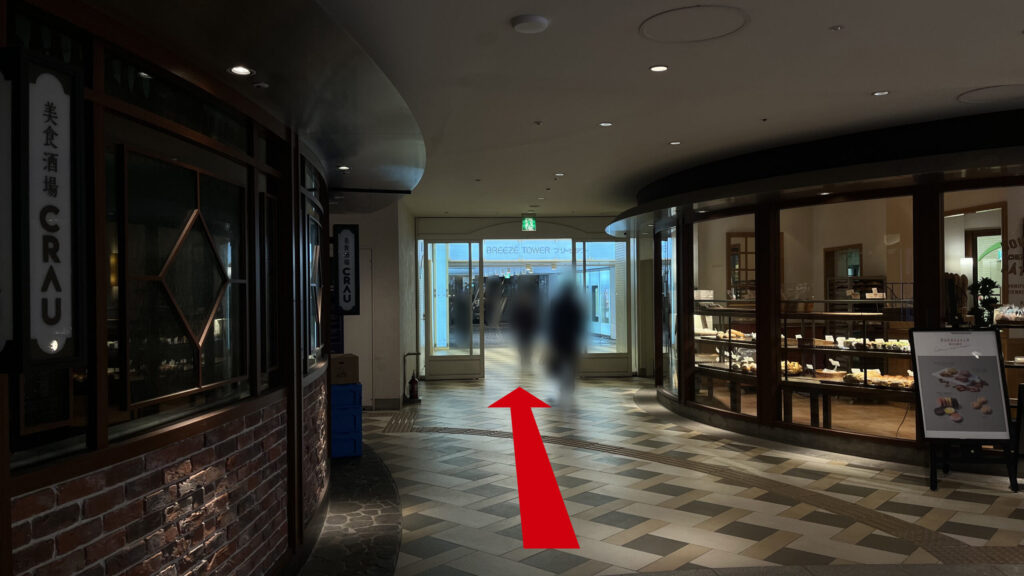 SYNTH×Business-Airport 西梅田ブリーゼタワーへのアクセス方法：左側にレンガ調の壁が続く飲食店街の地下通路。通路の突き当たりにガラス扉の入り口があり、上部に「BREEZE TOWER」と書かれた青いラインの看板が掲出されている。