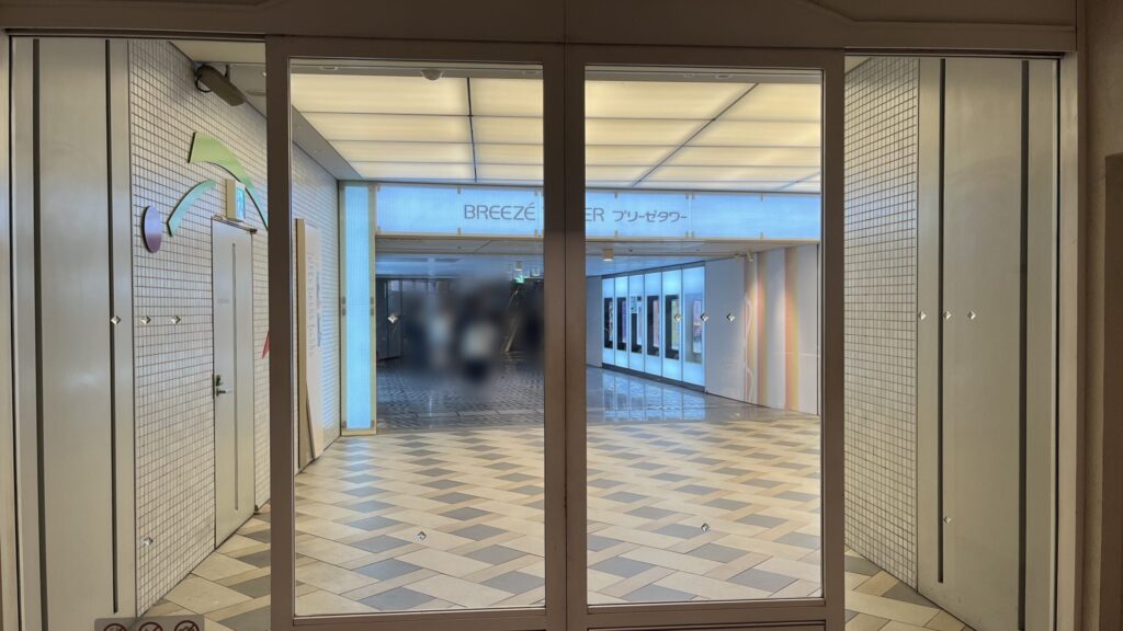 SYNTH×Business-Airport 西梅田ブリーゼタワーへのアクセス方法：ブリーゼタワー地下入口の正面。ガラス扉の上部に「BREEZE TOWER プリーゼタワー」の名称と施設ロゴがデザインされたバックライト式の看板が設置されている。