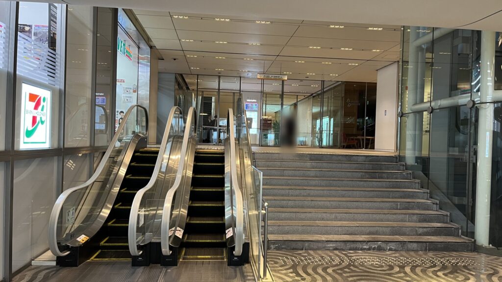 SYNTH×Business-Airport 西梅田ブリーゼタワーへのアクセス方法：連絡口を入ってすぐに現れるエスカレーターと階段。左手にセブンイレブン、右手に階段を上らないと利用できないエレベーターがある