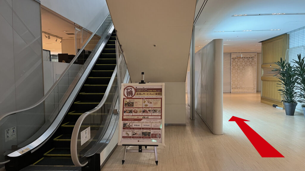 SYNTH×Business-Airport 西梅田ブリーゼタワーへのアクセス方法：ブリーゼタワー館内に入ってすぐにある下りエスカレーターの乗り口。エスカレーターの横には「チケ得」と書かれた赤いサービス案内の立て看板が設置されている。