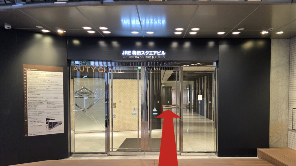 JRE梅田スクエアビルの地下連絡口　黒の壁にガラス扉、扉の上に「JRE梅田スクエアビル」と書かれたネオン看板が掲げられている　扉の左にテナント一覧が文字で書かれている