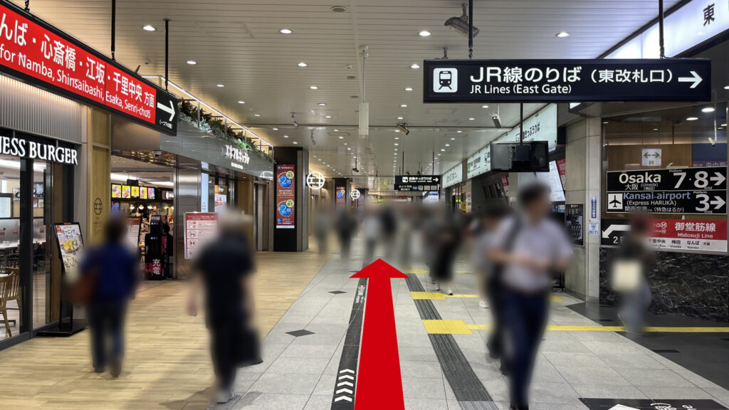 リージャス新大阪阪急ビルビジネスセンターへの行き方:JR線新大阪駅の東改札口を出た直後のコンコース。右方向へ誘導する頭上の案内看板があり、多数の歩行者が行き交っている。
