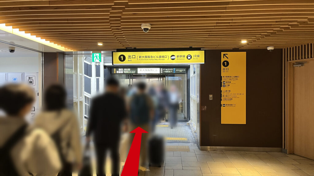 地下通路の天井部分。「1番出口(新大阪阪急ビル連絡口)」と書かれた黄色い案内看板が大きく設置されており、直進方向を指し示している。