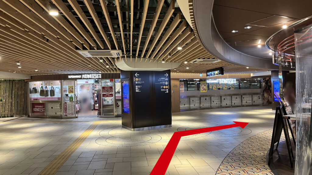 木目のルーバー天井が続く地下通路。左奥には成城石井の店舗があり、中央に置かれた案内柱の右側を抜けるように通路が延びている。