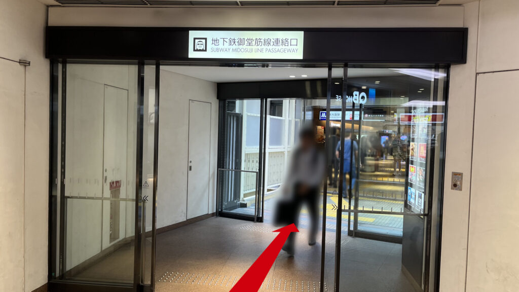 頭上に地下鉄御堂筋線連絡口と書かれた案内看板があるガラス扉の出入り口の様子。