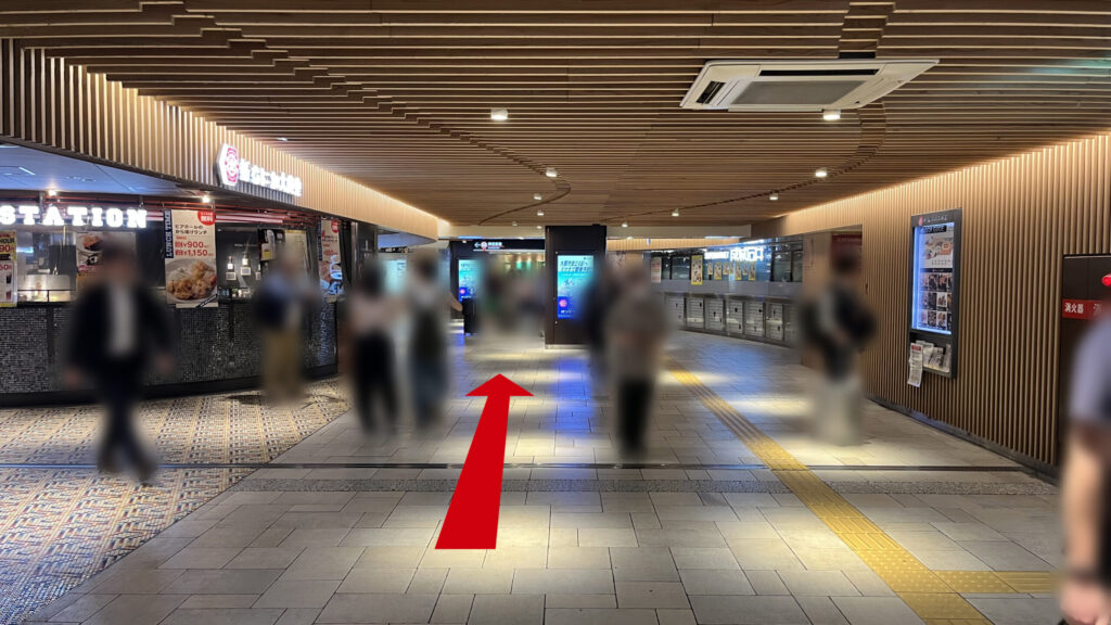木目調の天井が特徴的な地下通路で、左側に新なにわ大食堂の看板があり、右側に成城石井の店舗が並ぶ通路の様子。