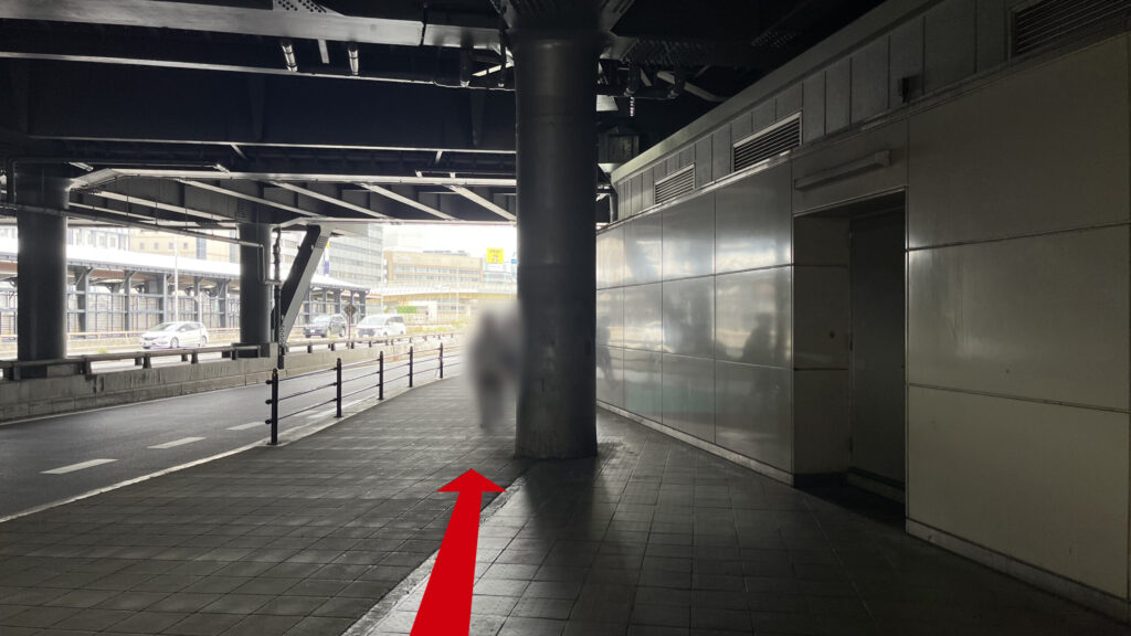 6番出口を上に上がった時に見える景色　高架下の薄暗い通路が見える　左側に新御堂筋があり、車が走っている　右側には壁がある