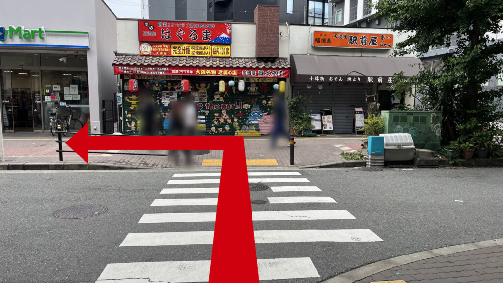 横断歩道付近の写真　反対側の歩道沿いに「駅前屋」「はぐるま」と書かれた居酒屋、「ファミリーマート」が並んでいる