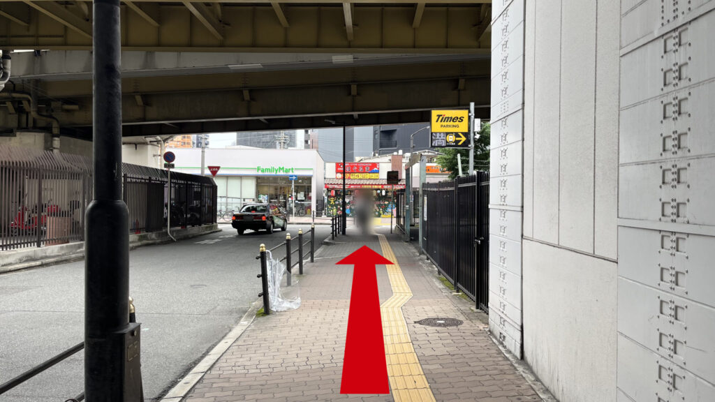 出口を出て右側に向いたときに見える風景　右側に「Times」の駐車場、左側に車道があり、茶色いタイルの敷かれた歩道が続いている　上には新御堂筋が横の軸で走っている