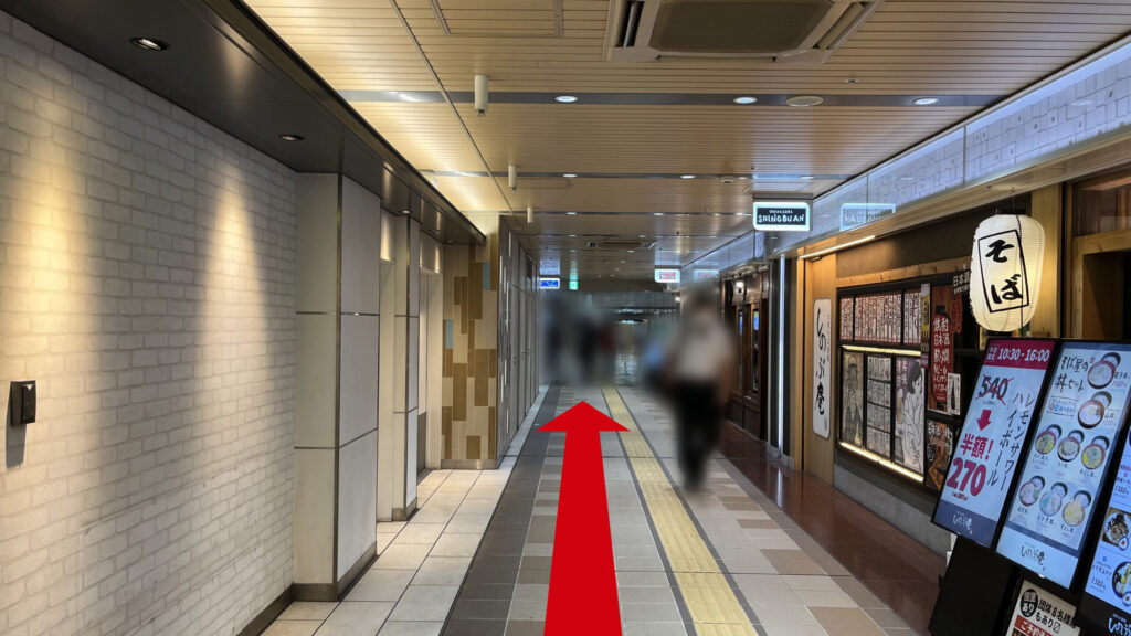 飲食店の通路。左には壁、右には「そば」という提灯がぶら下がった飲食店が写っている