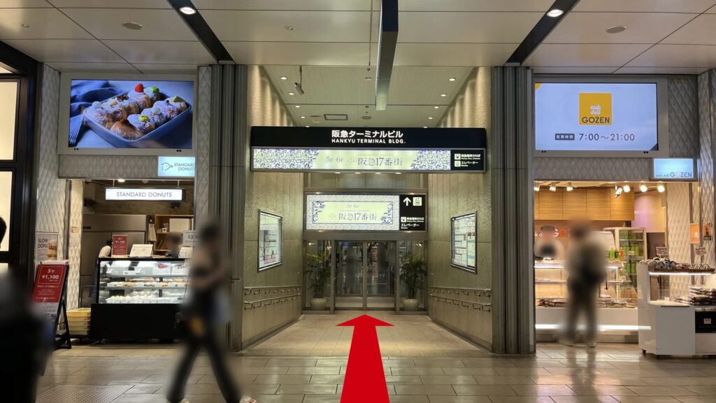 リージャス阪急ターミナルビジネスセンターの1F入口外観　左右に飲食店があり、頭上に「阪急ターミナルビル」「阪急17番街」と書かれた看板が掲示されている　スロープの通路が奥に続いている