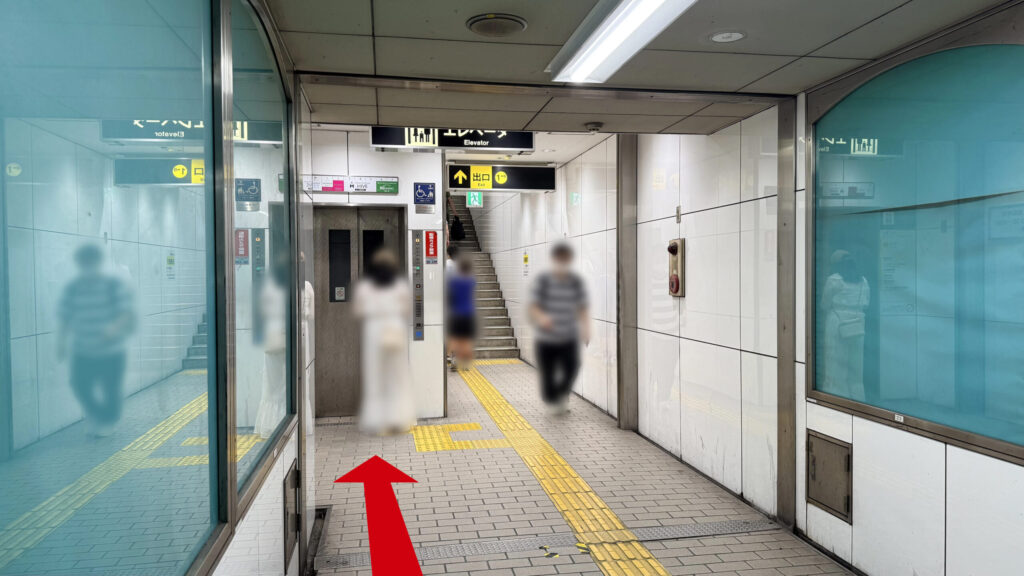 Alt:通路の突き当たりにある「出口1-B」へ続く階段と、その左側にあるエレベーターの乗り口。上部には「エレベーター Elevator」と書かれた黒い案内看板が設置されている。
