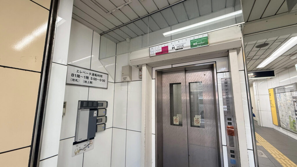 地下1階のエレベーター乗り口の様子。ドアの上部にはフロア案内があり、「3 4 5 Namba Guesthouse HIVE」「6 7 コワーキングスペース・レンタルオフィス BIZcomfort」と表示されている。