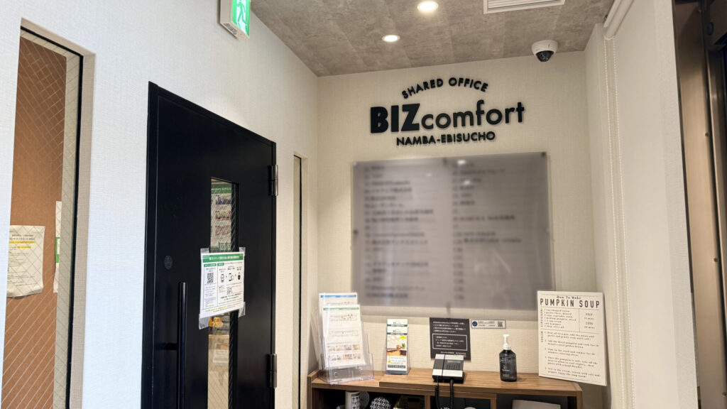 3階のエレベーターホール正面にある「BIZcomfort NAMBA-EBISUCHO」の黒いロゴマークが壁面に設置されたオフィス入口。黒い扉の横にはインターホンが設置されている。