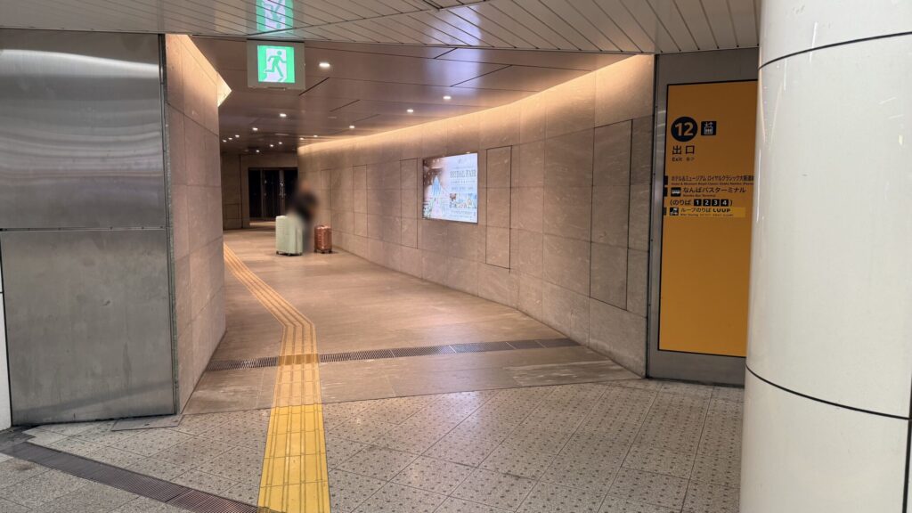 地下通路の様子。右側に黄色地に黒字で「12 出口」と記載された大きな案内板があり、奥へと続くまっすぐな通路が伸びている。