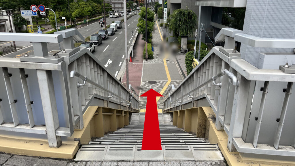 歩道橋から地上へ続く金属手すり付きの階段。階段の先には黄色の点字ブロックが敷かれた歩道が見える。