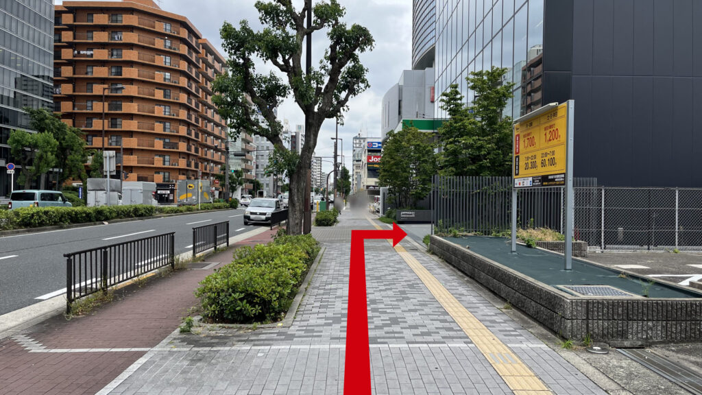 黄色の案内看板が設置されたコインパーキングの敷地と、その隣に建つ「H¹O 新大阪」の建物の外観。