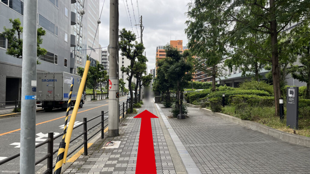 進行方向を向いた写真 左側にはビルと道路と電柱、中央と右側には歩道、右にはさらにビルがある タイル上の道が先まで続いている