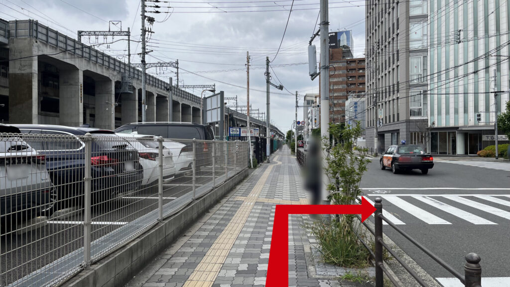 左手に駐車場フェンス、中央に歩道、右側に横断歩道が見切れている。