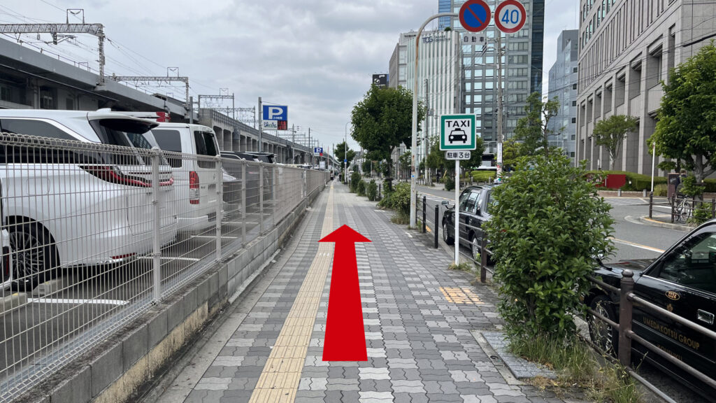 左手にフェンスで囲まれた駐車場と新幹線の高架があり、隣には舗装された車道と歩道があります。