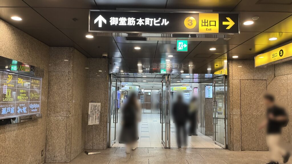ZXY本町への行き方:正面に御堂筋本町ビルB1Fエントランス、左に御堂筋本町ビルのテナント一覧、右に3番出口行きの黄色い看板が掲示された写真