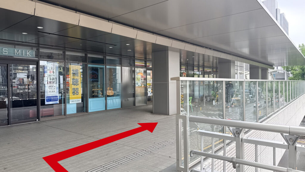 ガラス張りの「PARIS MIKI」店舗前と右側に広がるデッキ通路の様子。床面に点字ブロックが敷かれている。