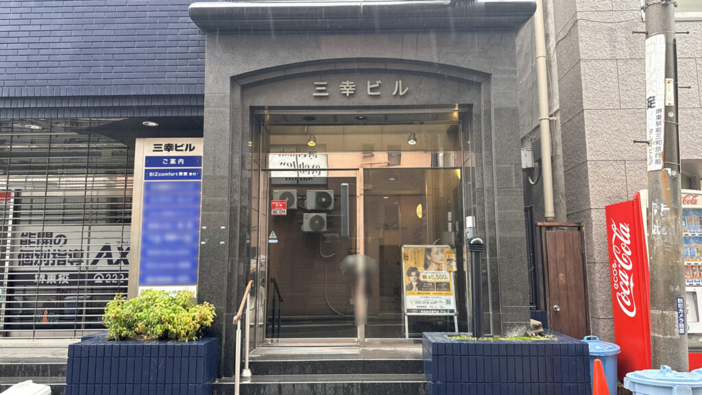 黒い石張りの「三幸ビル」のエントランス部分の様子。正面にガラス扉の入口がある。