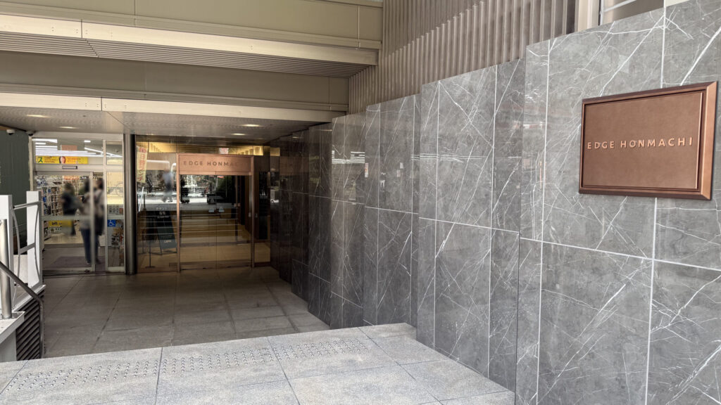 EDGE HONMACHIの金属製銘板とビル内部へ続くガラス扉の通路