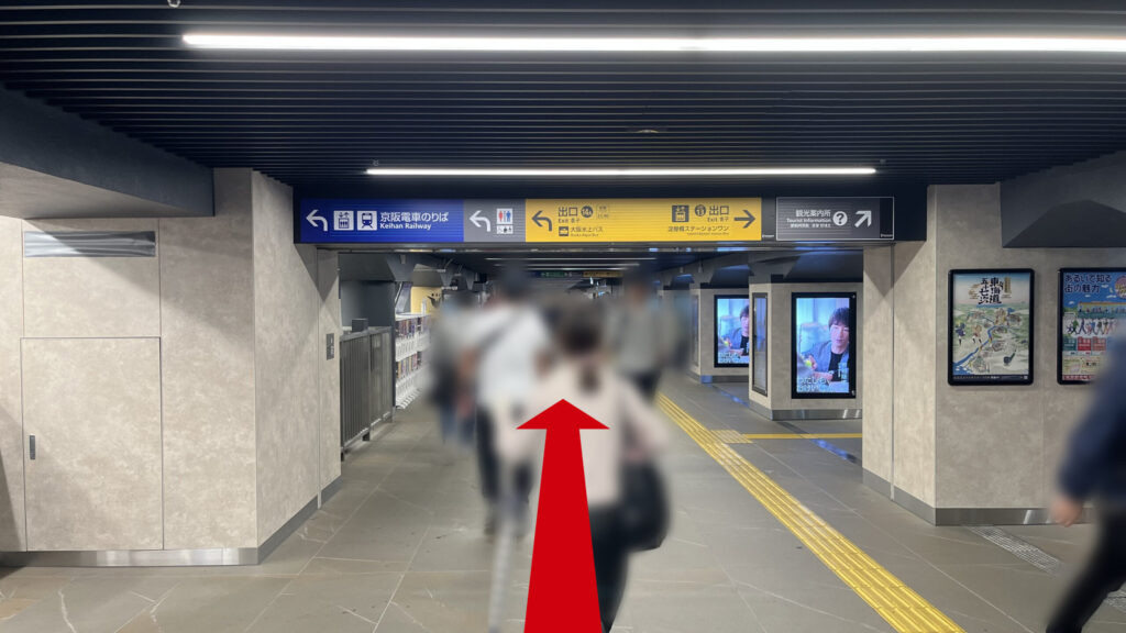 京阪淀屋橋駅と御堂筋線淀屋橋駅がクロスするあたりを東に向いた様子　頭上に京阪電車乗り場や出口、観光案内所などの案内板が貼られており、その下に通路が伸びている